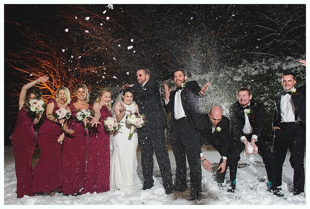 Wedding party in snow, throwing snow up; bride in white gown, bridesmaids in burgundy.