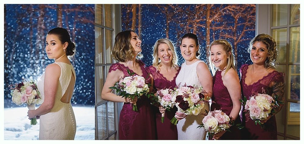 Bride and bridesmaids in dresses, holding bouquets, by window with snowy, outdoor scene.
