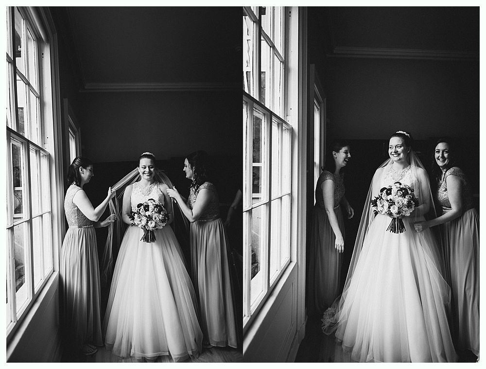 Bride in wedding dress with bridesmaids, near a window. Black and white photo.