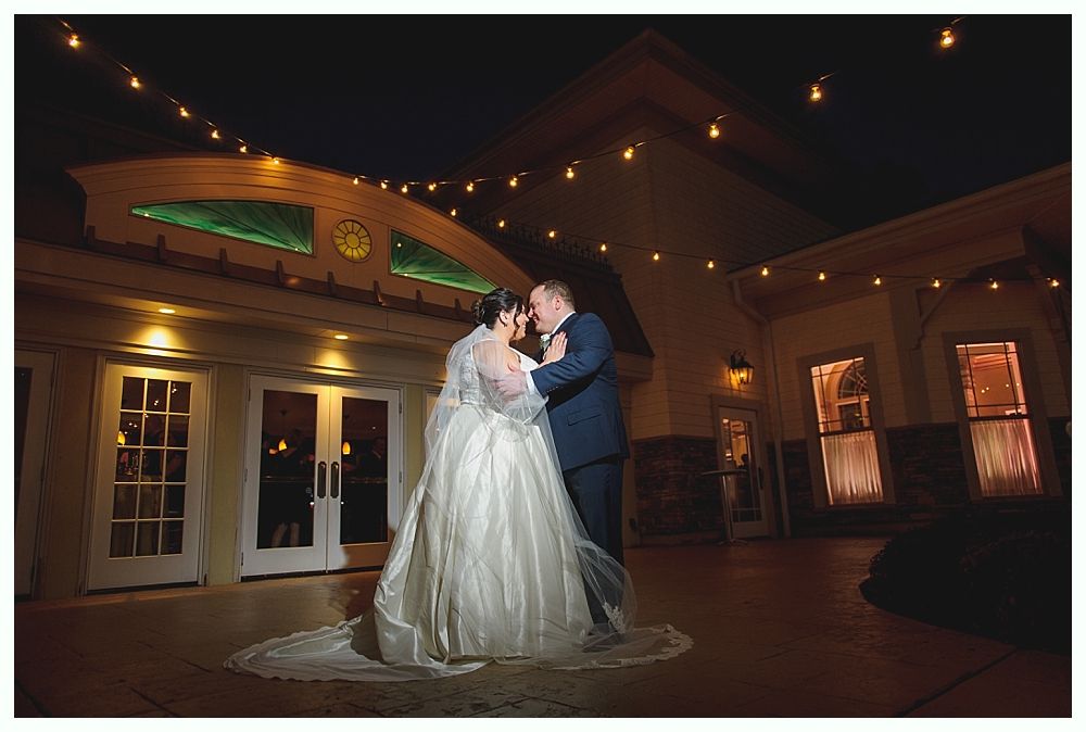 Couple dancing at night under string lights in front of a building with arched windows.