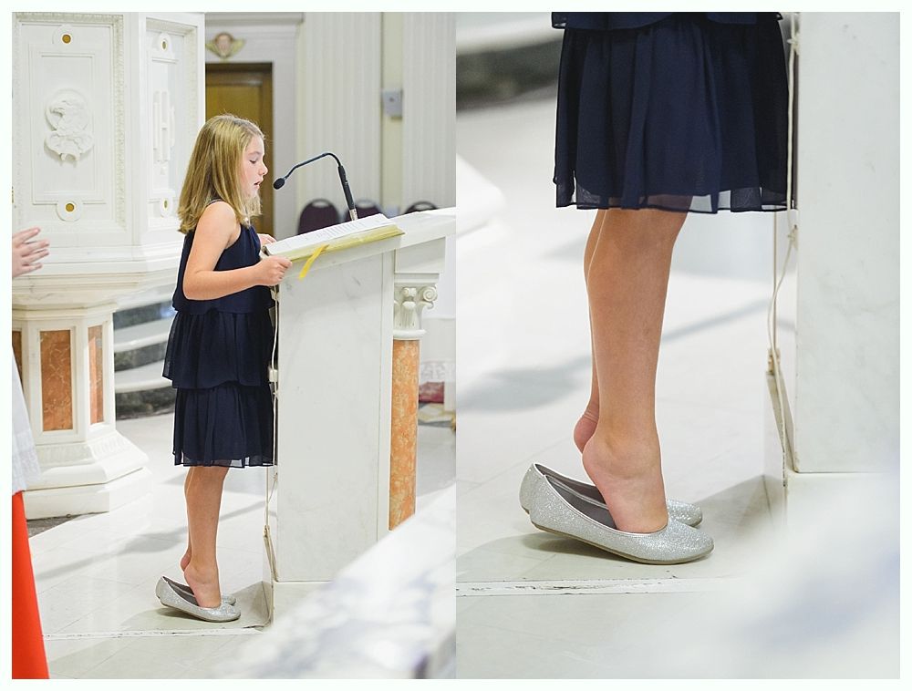 Girl in blue dress standing at a lectern, using her foot to stabilize a shoe, church interior.