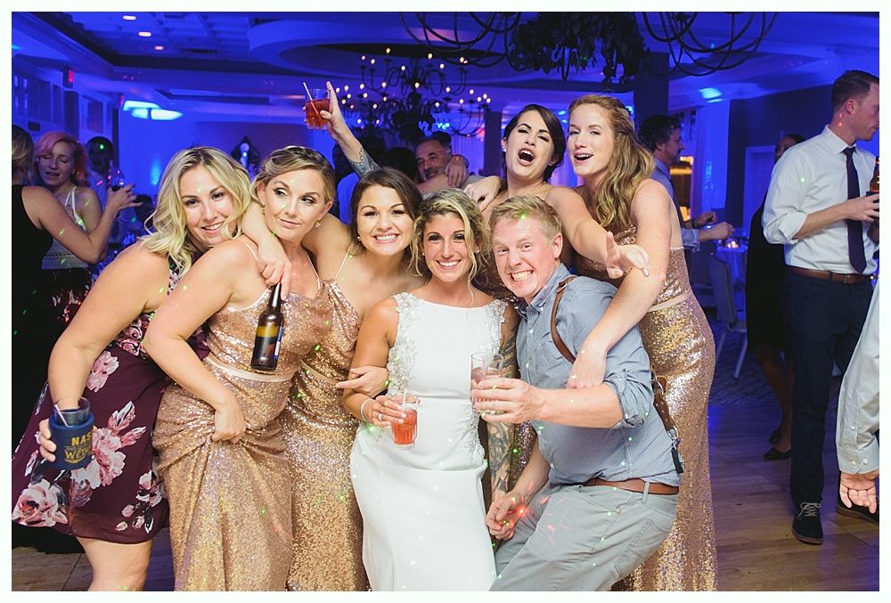 Group of people at a wedding reception, some in gold dresses, smiling and posing.