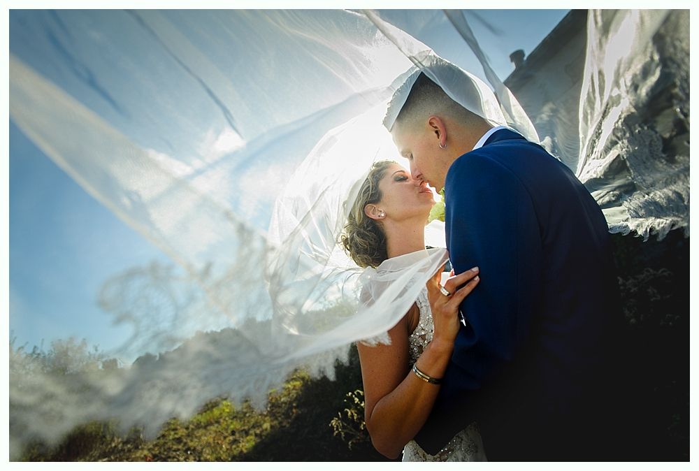 Couple kissing under a veil, sun shining through. Outdoors, romantic moment.