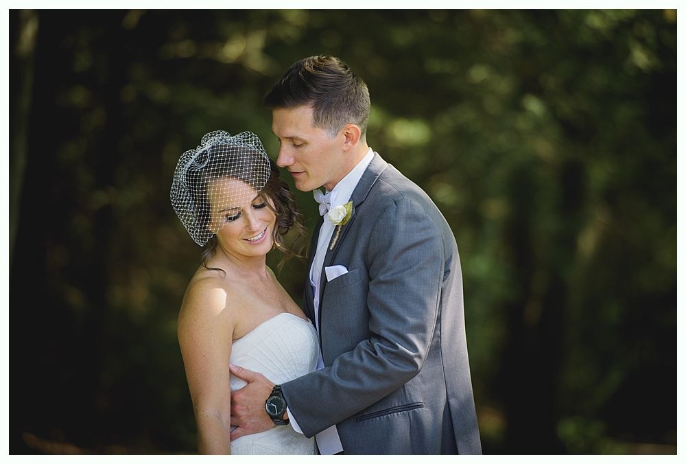 Bride and groom embrace outdoors; she wears a strapless white dress and a veil, he wears a gray suit.