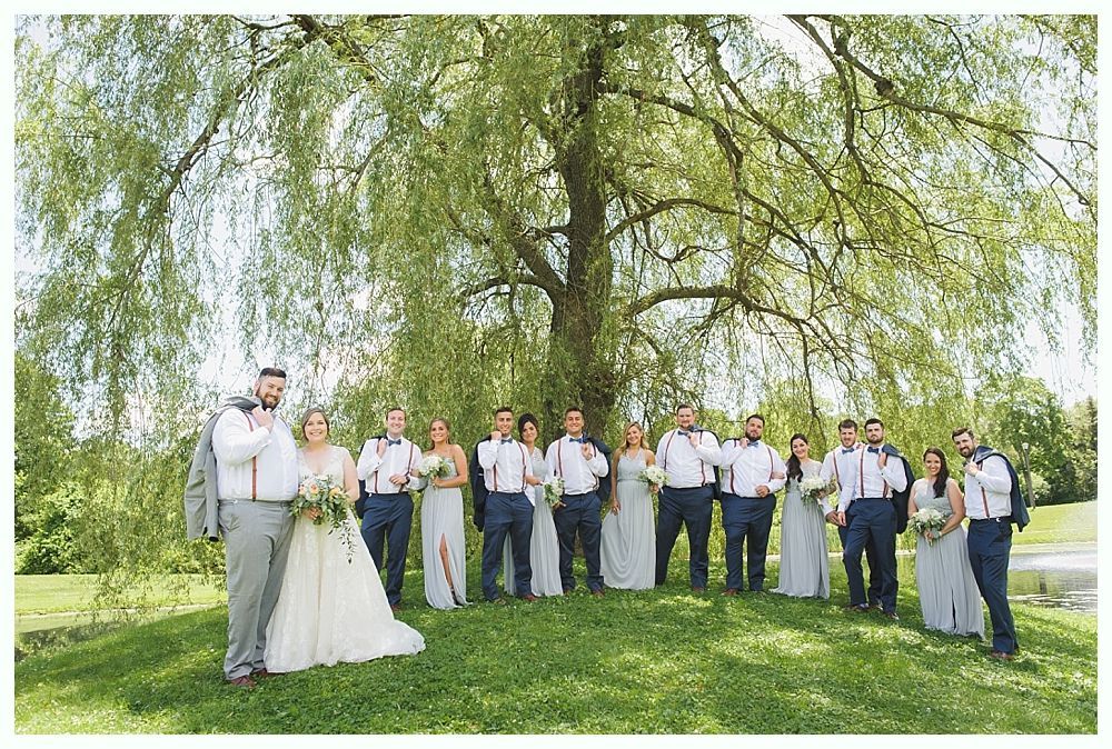 Wedding party poses under a weeping willow tree. Bride, groom, and bridesmaids/groomsmen in formal attire.