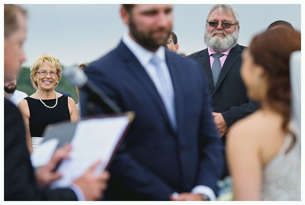 Wedding ceremony: Attendees watch as officiant speaks. Bride and groom stand, facing each other.