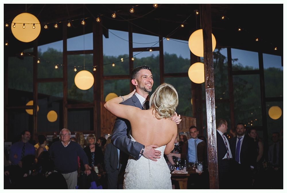 Couple dancing at a wedding reception, lit by string lights and round lanterns, surrounded by guests.