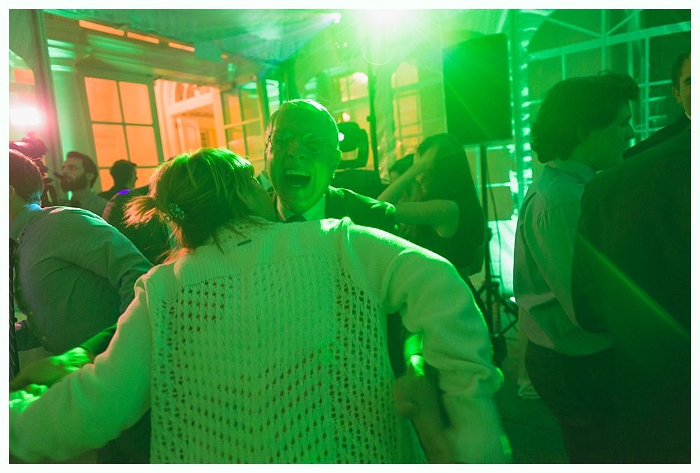 People dancing at a party under green and orange stage lights.