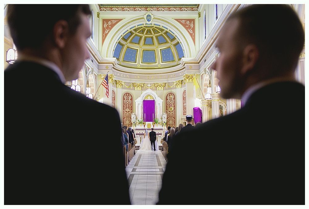 Two men in suits look down the aisle of a church at a person standing at the altar.