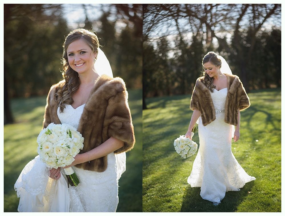 Bride in a white gown and fur wrap, holding a bouquet, standing in a sunny garden.
