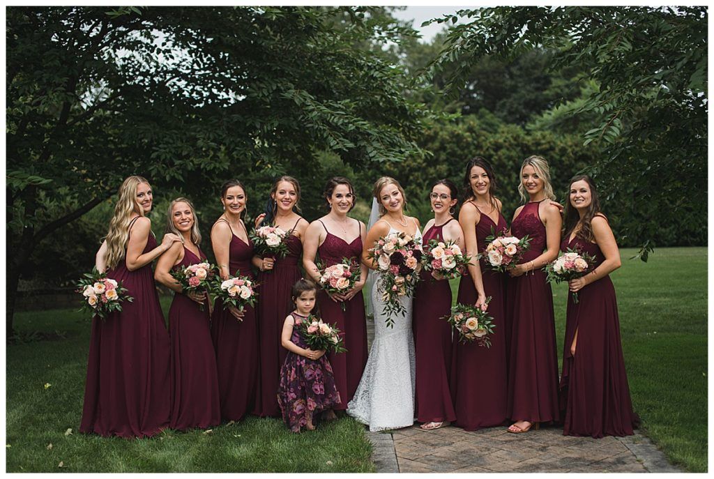 Wedding party in burgundy dresses and bride in white dress, outdoors.