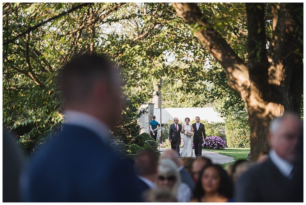 Bride walks down aisle with father; outdoor wedding.