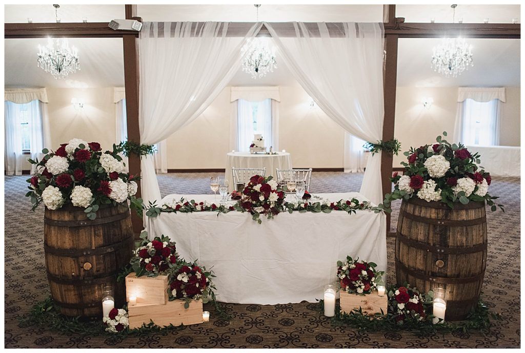Wedding reception table decorated with flowers, draped fabric, and barrels.