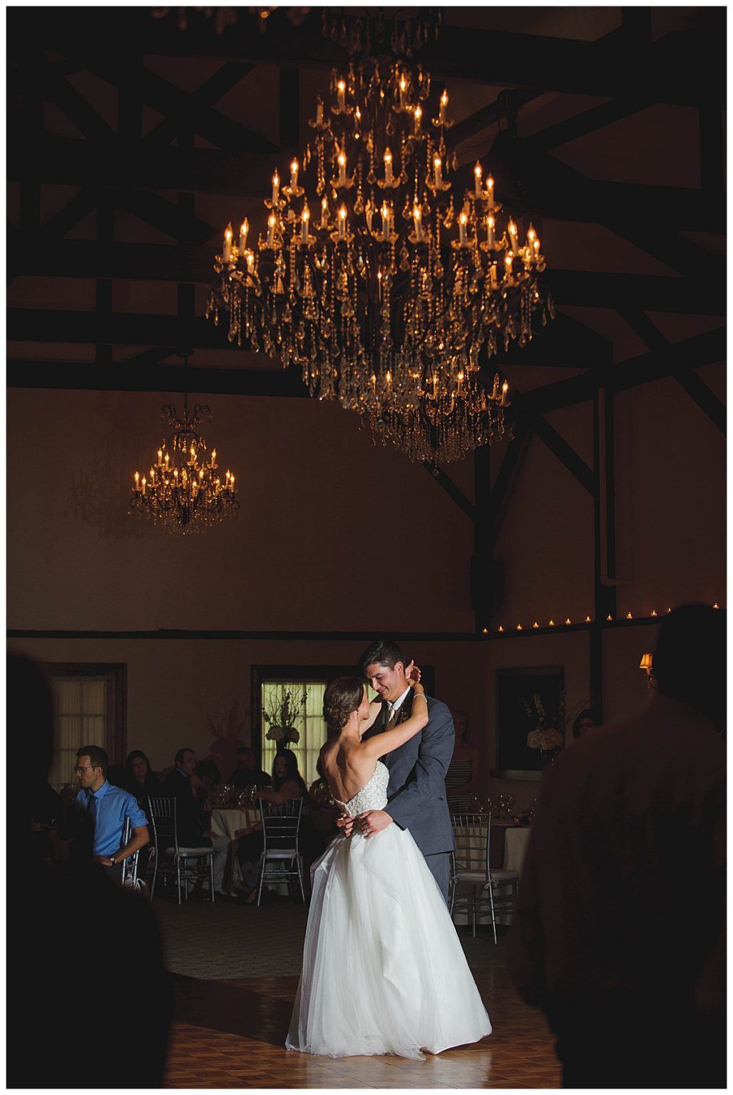 Bride and groom dance under a large chandelier at a wedding reception.
