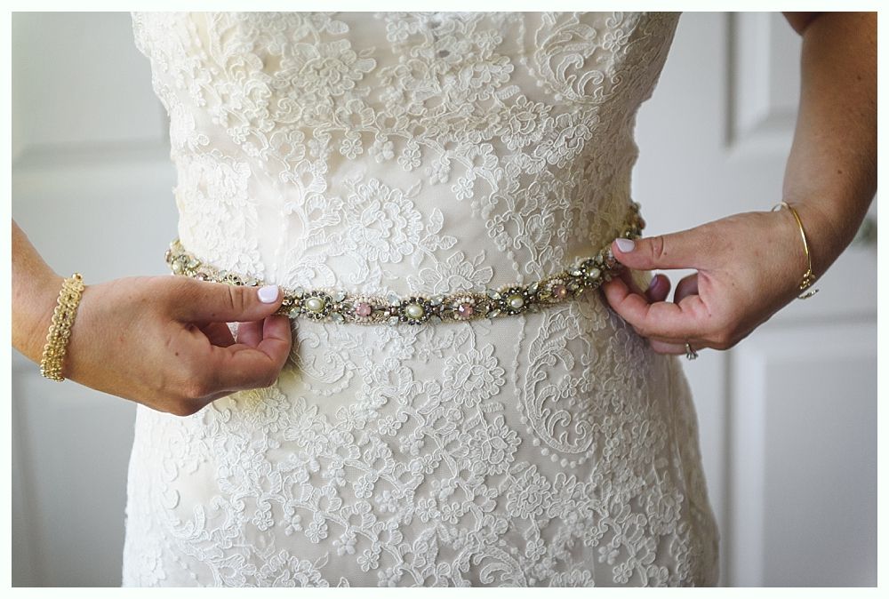 Woman adjusting a beaded belt on her lace wedding dress.