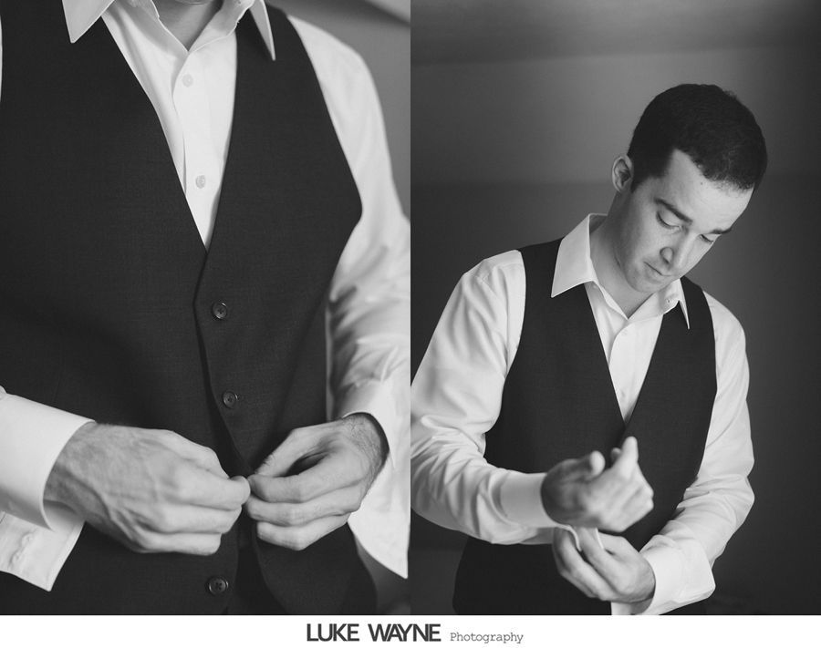 Man buttoning a vest over a white shirt, preparing for an event.
