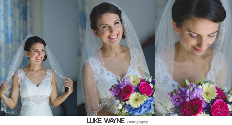 Bride holding a colorful bouquet, wearing a veil and lace dress, smiling in a well-lit room.