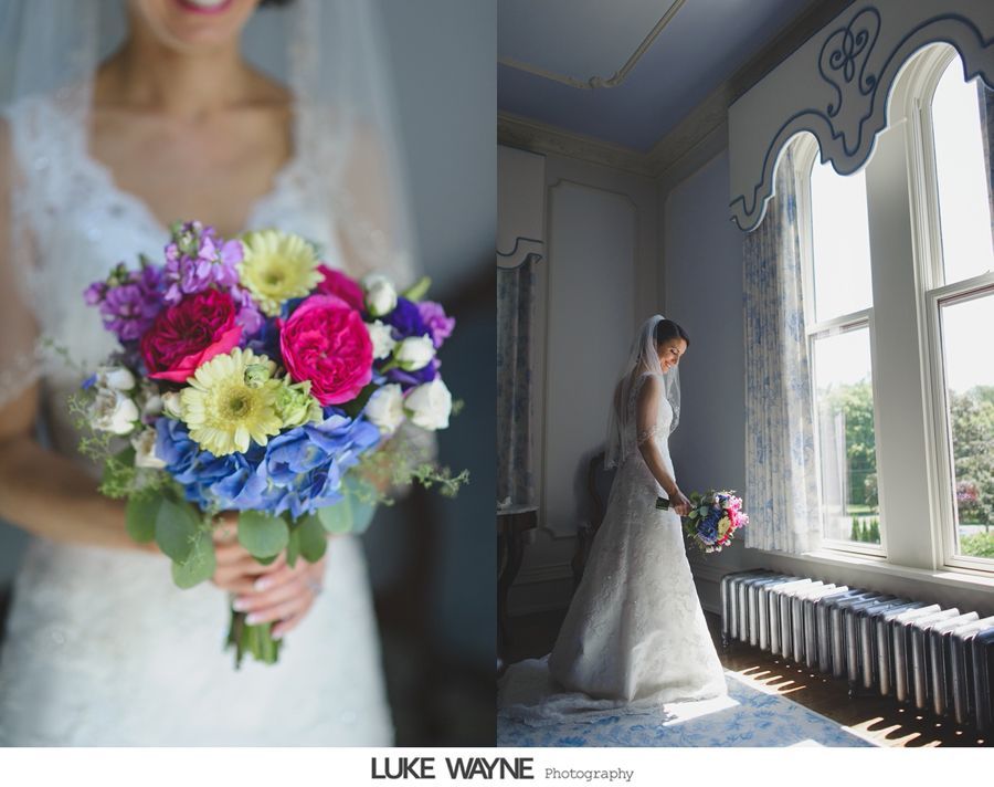Bride holding colorful bouquet, standing by a window in a bright room.
