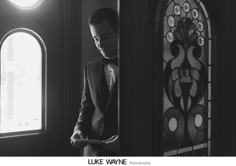 Man in suit reads a letter, standing in a doorway with stained glass and arched window. Black and white.