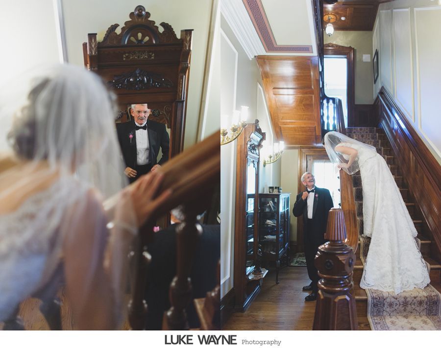 Bride descending stairs to groom in a vintage house, veil covering her face. Groom smiles.