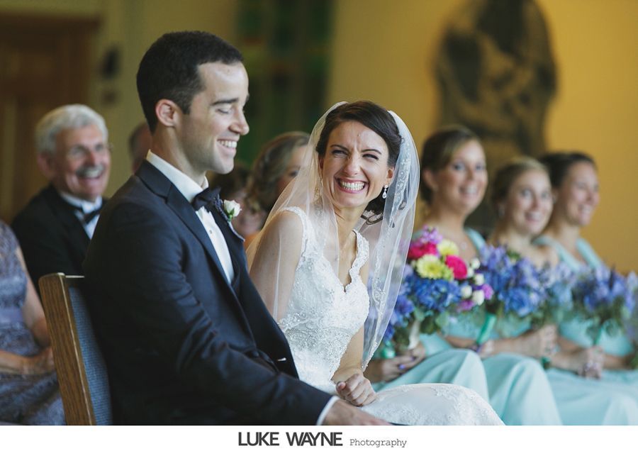 Couple smiling at wedding ceremony, bride in lace dress, bridesmaids in teal.