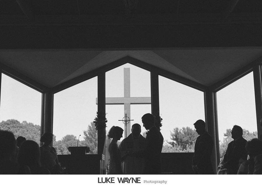 Wedding ceremony silhouette with couple, officiant, and guests in a church; cross visible in window.