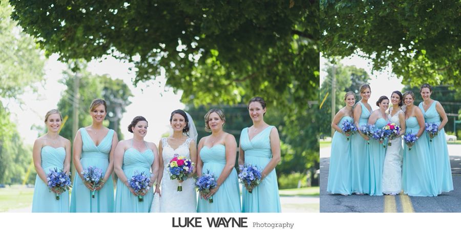 Bridesmaids in teal dresses and bride in white, holding bouquets, under a green tree.