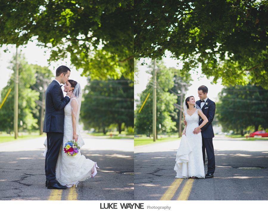 Wedding couple embraces in a road under a tree canopy. Bride in white dress and groom in suit.