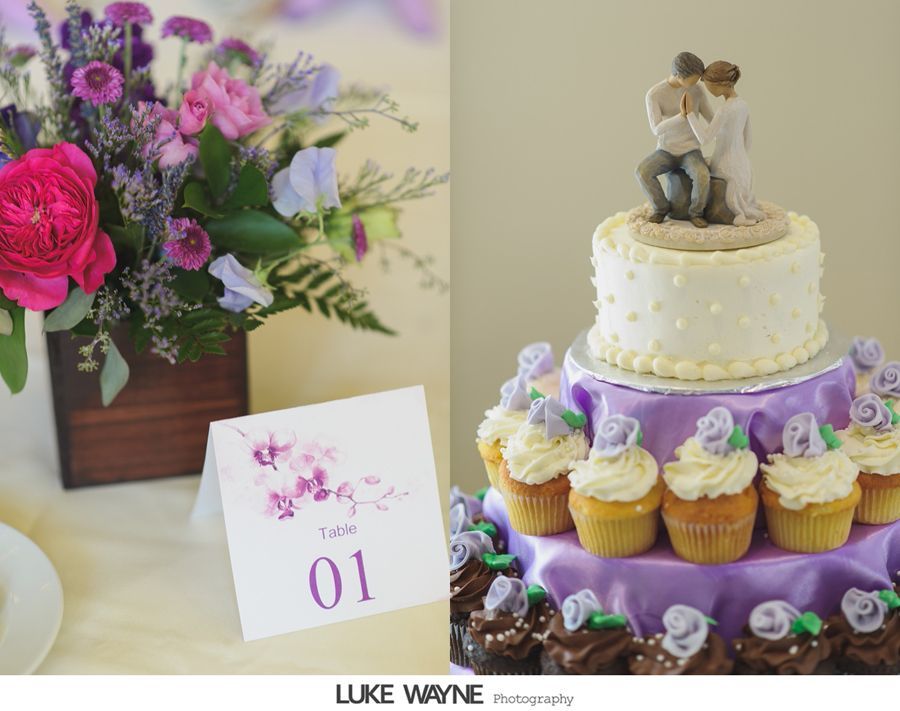 Wedding reception decor with floral arrangement, table number, and tiered cake with cupcakes.