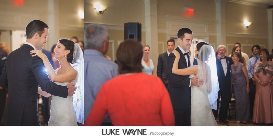 Bride and groom dance at a wedding reception. People watch in a ballroom with a neutral color scheme.