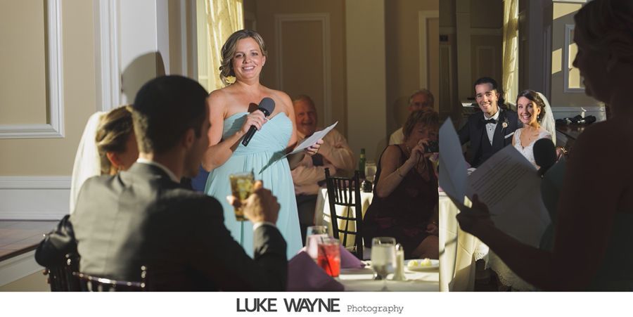 Woman in a blue dress gives a speech at a wedding. The bride and groom smile in the background.