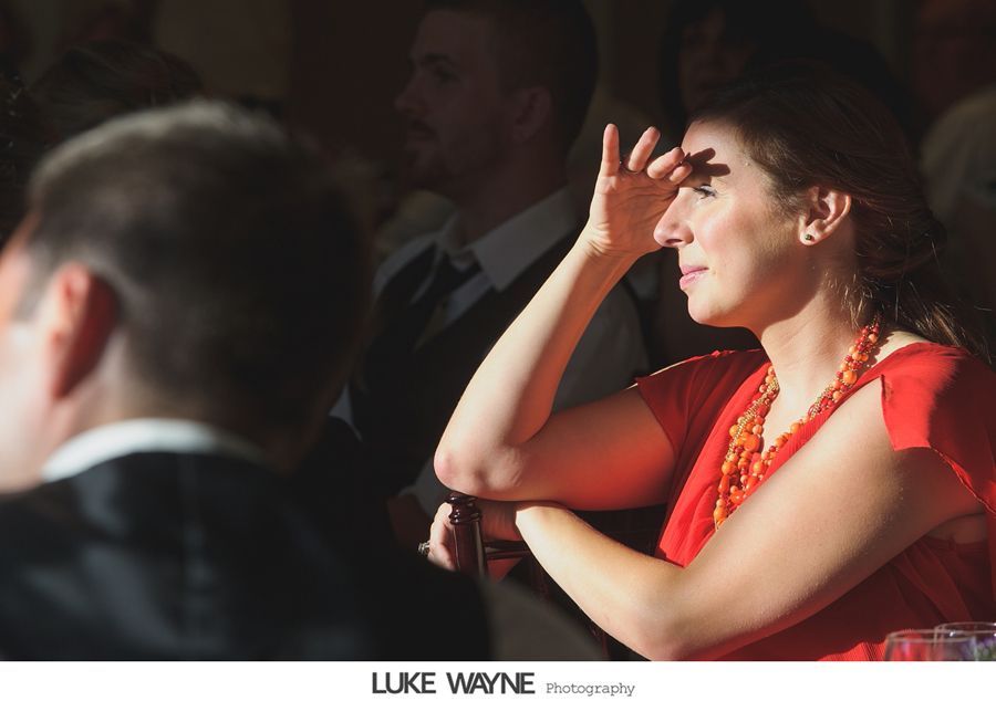 Woman shielding eyes in red dress, attending an event, with people in the background.