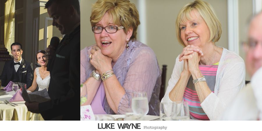 Wedding guests react to a speech. A woman in glasses and a purple shawl laughs, and another woman smiles.