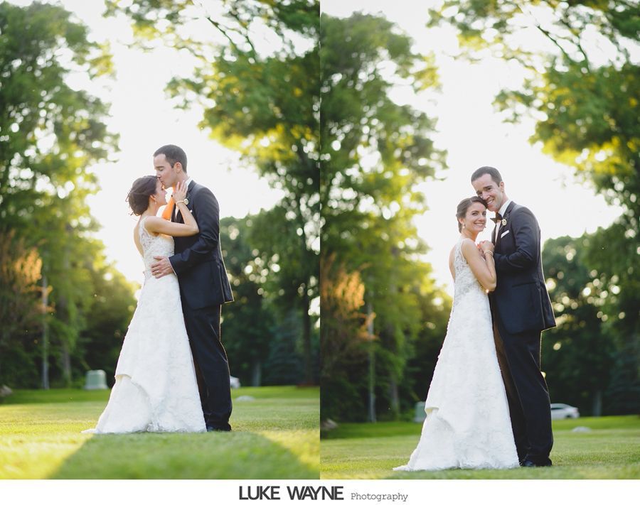 Bride and groom embrace on a grassy lawn with trees in the background, sunlit wedding photo.