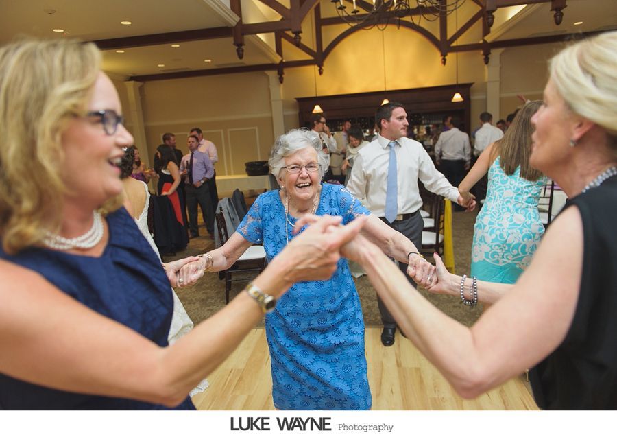 People dancing in a circle at a wedding reception. Woman in blue dress smiling, holding hands with others.
