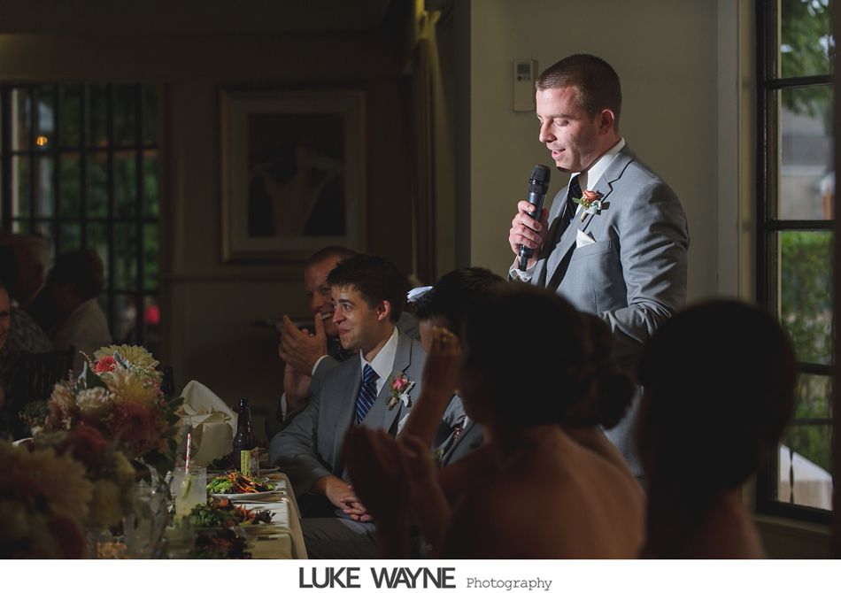 Man in gray suit gives a speech at a wedding reception.