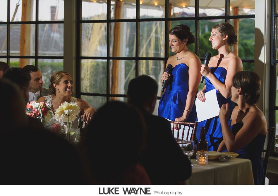 Two women in blue dresses giving a speech at a wedding, bride smiling.