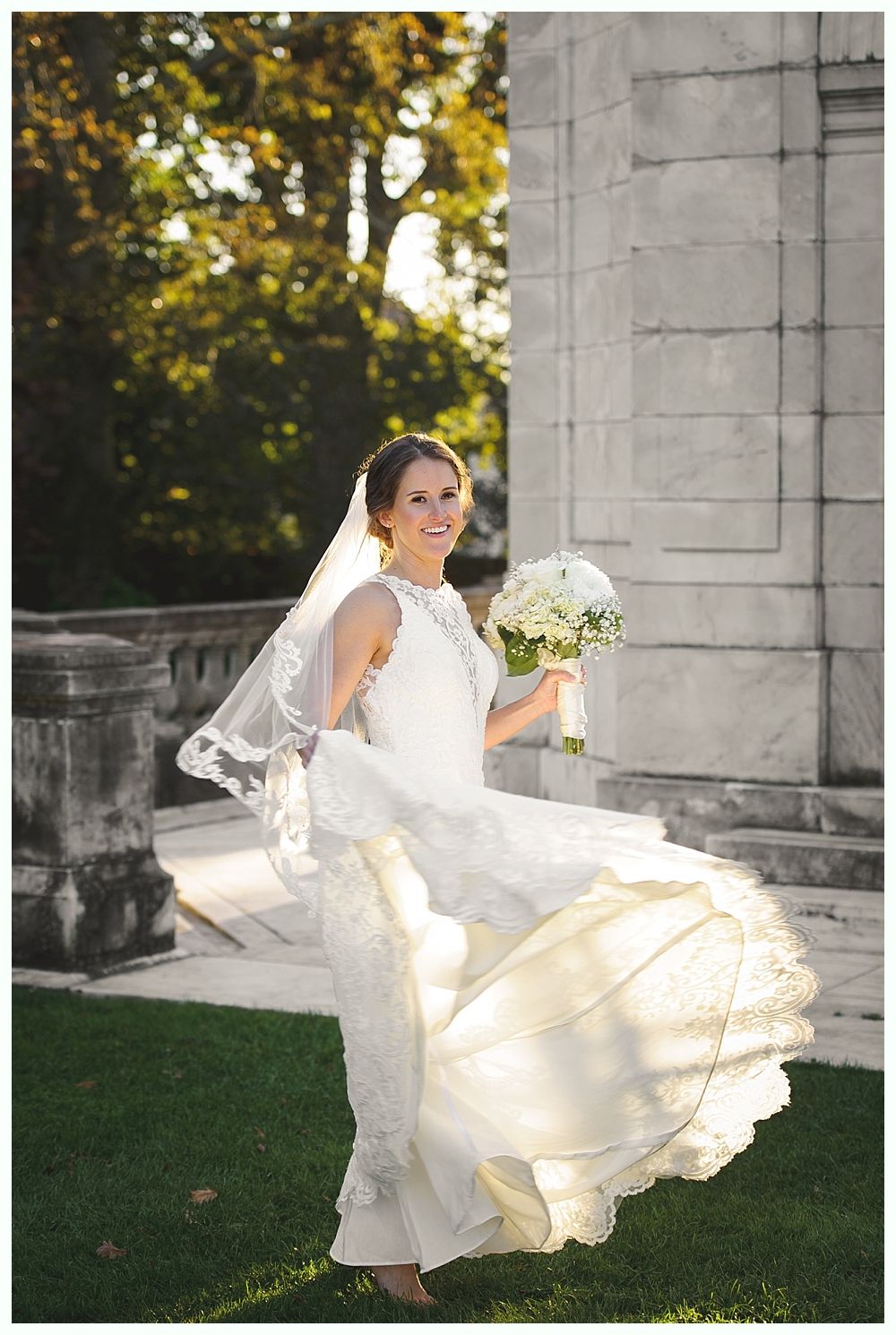 Bride twirling in wedding dress, holding bouquet, outdoors near a stone building.
