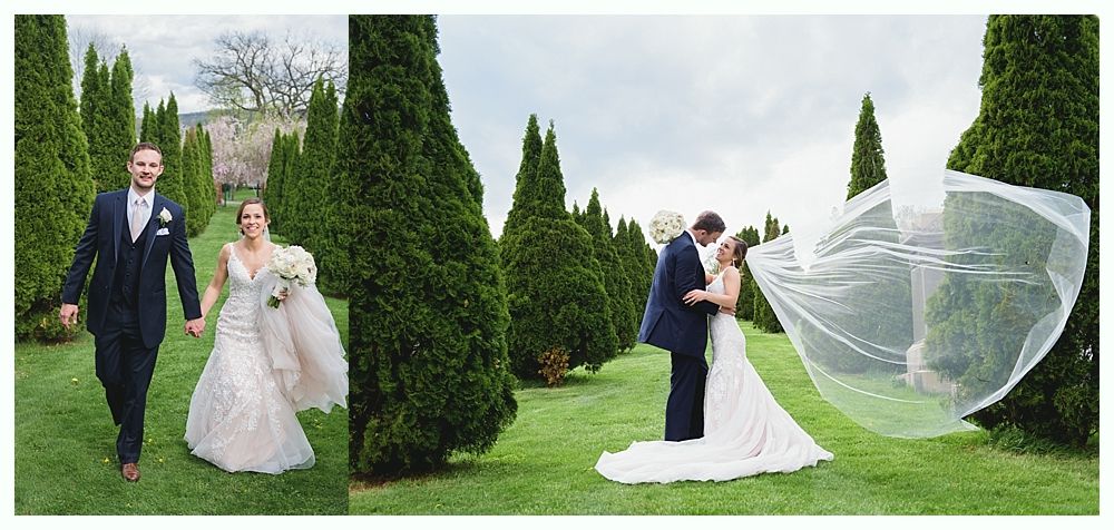 Wedding photos: Couple walking, kissing, bride's veil blowing in wind, tall green trees, green lawn.