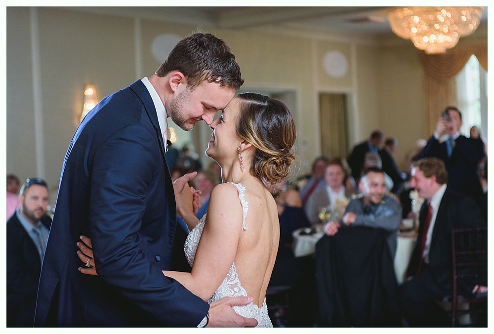 Couple dancing close at their wedding reception; guests in background.