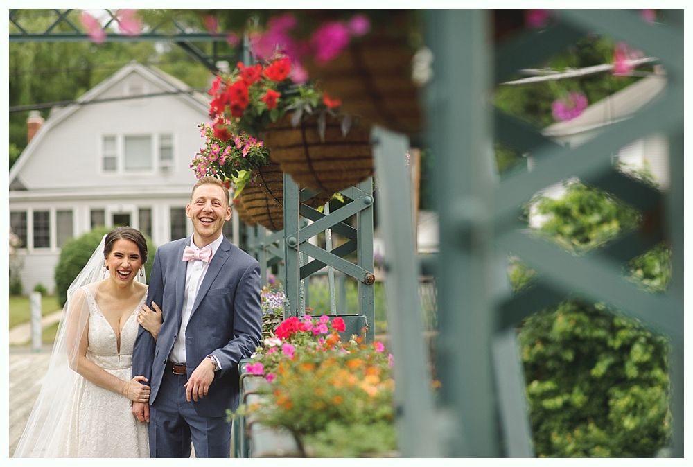 Bride and groom smile, posing by flower boxes near a building.