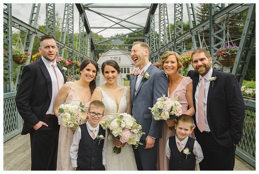Wedding party on a metal bridge. Bride & groom, bridesmaids, groomsmen, and children smiling with bouquets.