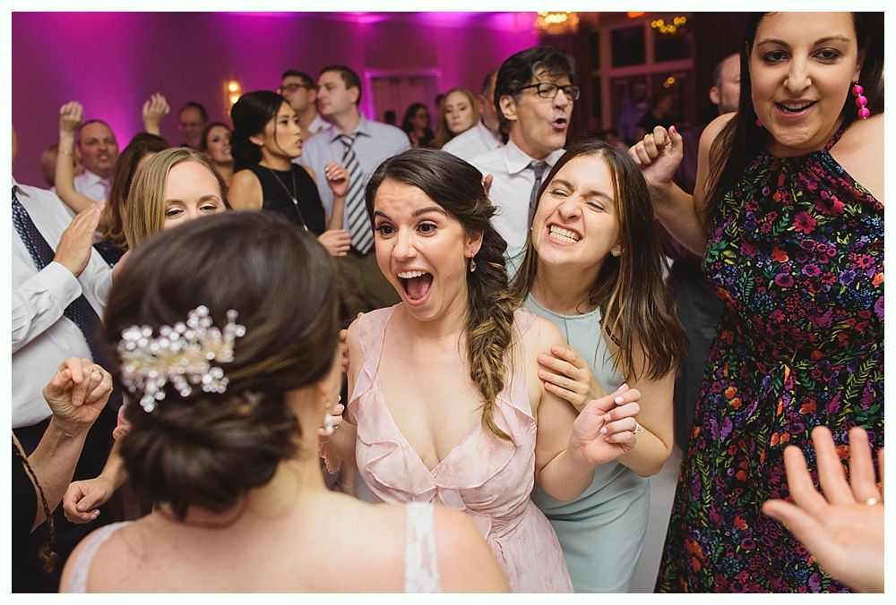 People dancing at a party; woman in pink dress is smiling widely, other guests are visible.
