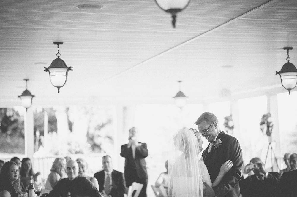 Bride and groom dancing, in a ballroom with draped windows. The groom wears a suit; the bride a strapless dress.
