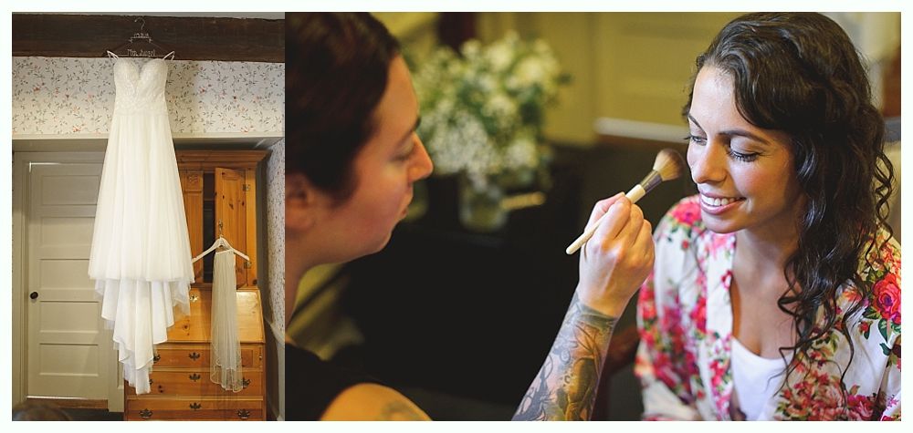 A wedding dress hangs near a doorway. A makeup artist applies makeup to a smiling woman.