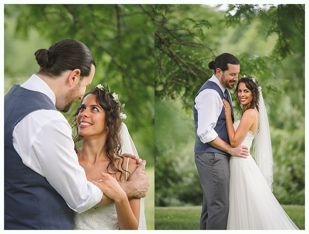 Bride and groom embrace outdoors, she in a white dress and veil, he in a blue vest, both smiling.