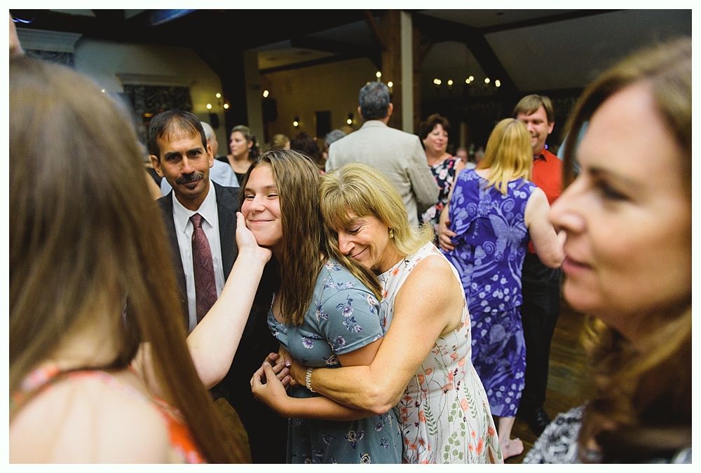 People hugging and smiling on a dance floor, with a man looking on.