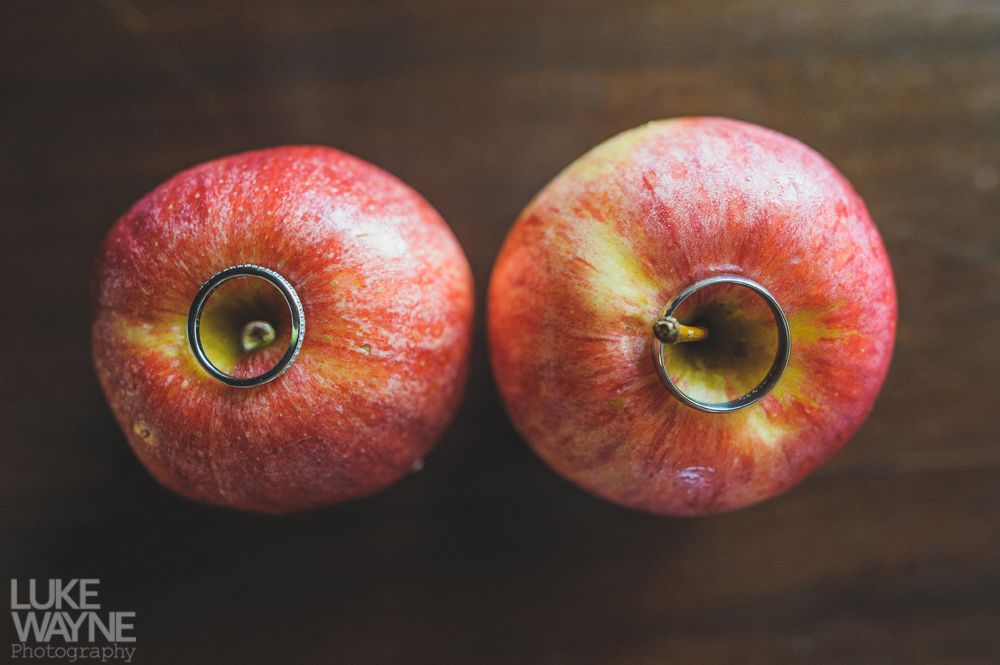 Two red apples with wedding rings inserted into their core, on a wooden surface.