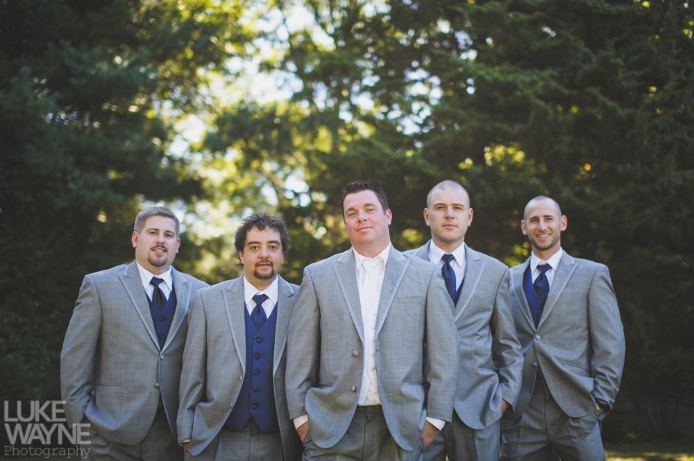 Five men in gray suits and blue ties pose outdoors in front of trees.