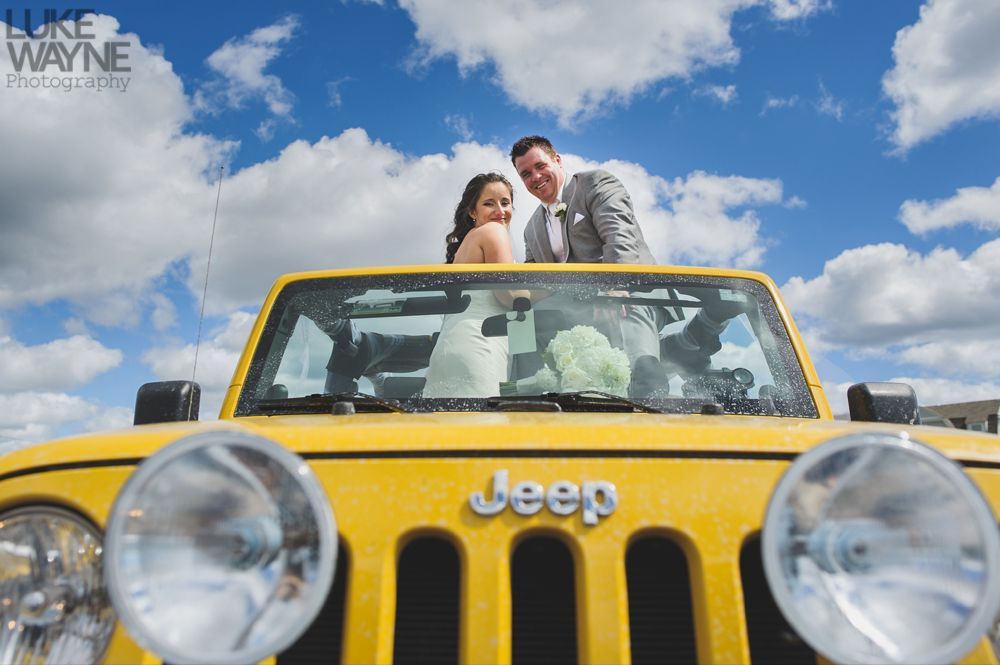 Bride and groom in a yellow Jeep, smiling at the camera against a bright blue sky.